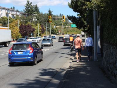 Image of people walking, a person riding a bike and people driving along Island Highway near 4 Mile Road. 